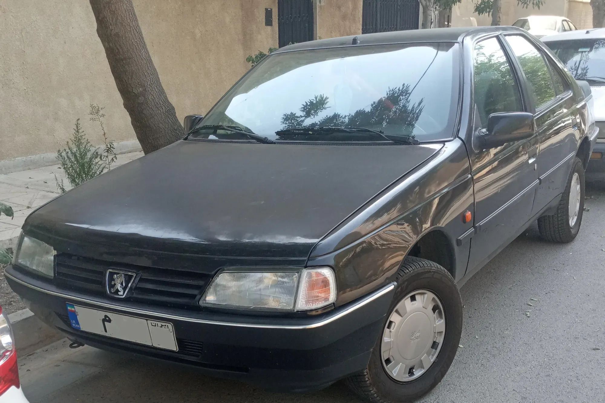 پژو ۴۰۵ مشکی از جلو و پهلو، پارک‌شده کنار پیاده‌رو و دیواری کاهگلی